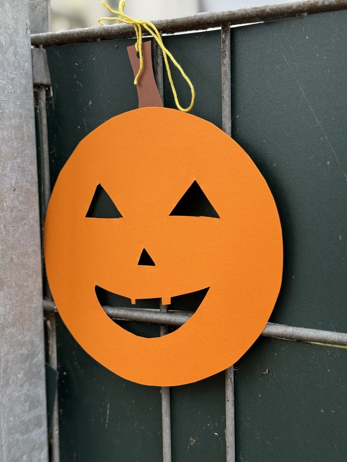 Gebastelter orangefarbener Kürbis aus Papier an einem grünen Zaun